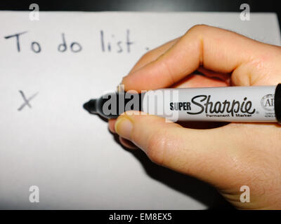 Una mano bianca tenendo un pennarello indelebile Sharpie pen scrivendo un 'Lista da fare su un foglio di carta. Foto Stock