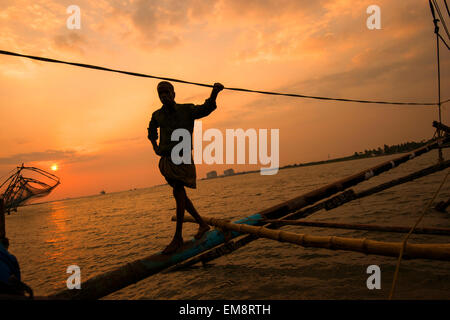 Un pescatore in silhouette al tramonto, in piedi su un cinese reti da pesca in Fort Kochi, Kerala India Foto Stock