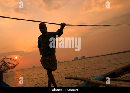 Un pescatore in silhouette al tramonto, in piedi su un cinese reti da pesca in Fort Kochi, Kerala India Foto Stock