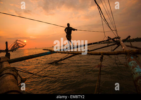 Un pescatore in silhouette al tramonto, in piedi su un cinese reti da pesca in Fort Kochi, Kerala India Foto Stock