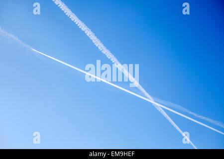 Piano di Jet contrails striature in un X configurazione attraverso un luminoso cielo blu. Foto Stock