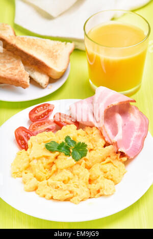 La prima colazione con uova strapazzate, pancetta, le fette di pomodoro, pane tostato e succo di arancia Foto Stock
