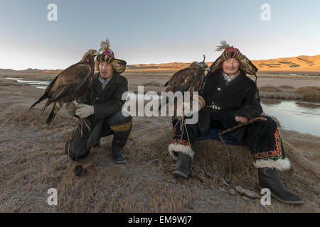 Due cacciatori kazako con loro le aquile reali di sunrise, Mongolia occidentale Foto Stock