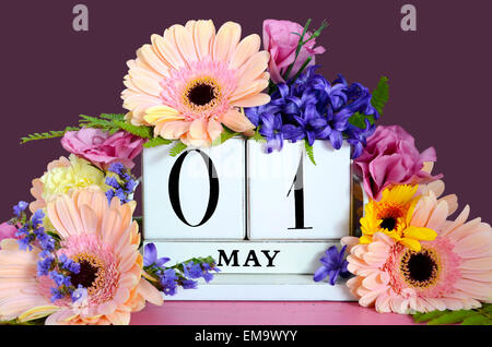 Felice giorno di maggio vintage calendario di legno decorate con fiori di primavera rosa sulla tavola di legno con viola scuro dello sfondo. Foto Stock