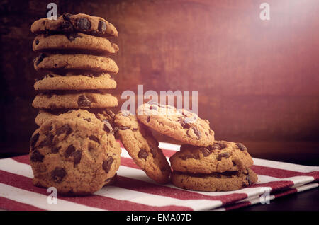 Pila di biscotti con scaglie di cioccolato sulla rossa e bianca igienico contro un legno scuro sfondo, con applicata in stile vintage filtro Foto Stock