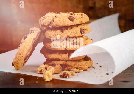 Pila di biscotti al cioccolato su bianco arricciatura carta da forno contro un legno scuro sfondo, con applicata in stile vintage filtri Foto Stock