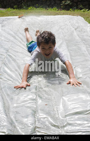 Sette anni di vecchio ragazzo gioca su una casalinga e slittamento slitta nel suo cortile interno con sua madre e 4 anno vecchio fratello Foto Stock