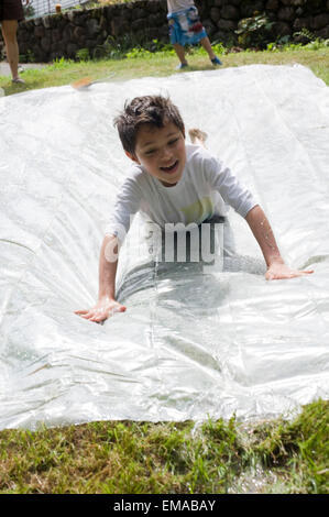 Sette anni di vecchio ragazzo gioca su una casalinga e slittamento slitta nel suo cortile interno con sua madre e 4 anno vecchio fratello Foto Stock
