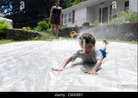 Sette anni di vecchio ragazzo gioca su una casalinga e slittamento slitta nel suo cortile interno con sua madre e 4 anno vecchio fratello Foto Stock