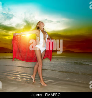 Donna con sarong rosso al tramonto vicino al mare Foto Stock