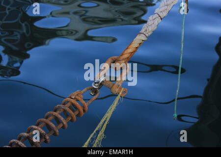 Metallo arrugginito il gancio e la corda che si collegano a una barca che si vede nella riflessione sulle calme acque del mare Foto Stock