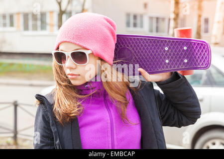 Bionda bella ragazza adolescente in occhiali da sole con lo skateboard, ritratto all'aperto Foto Stock