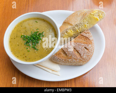 Café pranzo una ciotola di Zucchine Patate e zuppa di erbe e rabboccato con erba cipollina tritata con imburrato pane bianco Foto Stock