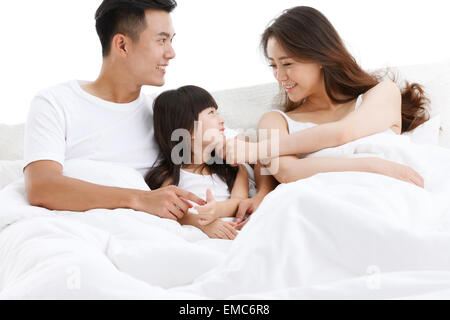 Una famiglia di tre seduti sul letto in camera da letto Foto Stock