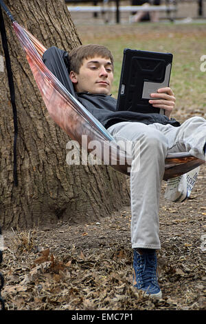 Uno studente di college su un amaca lettura dal suo ipad in Washington Square Park, Greenwich Village di New York City. Foto Stock
