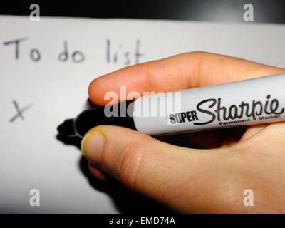 Una mano bianca tenendo un marcatore nero a scrivere un elenco delle cose da fare in carta bianca. Foto Stock