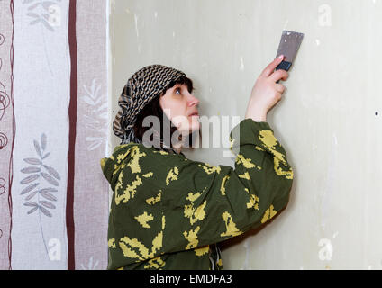 Donna raschiato la vecchia carta da parati fuori dalla parete Foto Stock