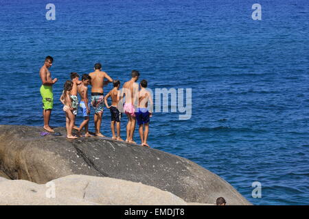 Gli adolescenti sono in piedi sulle rocce grigie in attesa di tuffarsi nelle acque blu di un'isola greca. Foto Stock