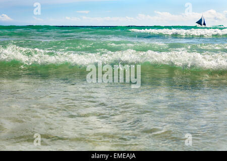 Bella vista sul mare blu con barca a vela e grandi onde bianco sul primo piano Filippine Boracay Foto Stock