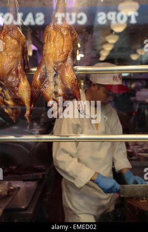 L uomo nella preparazione degli alimenti all'interno di una finestra di un ristorante cinese nella Chinatown di Manhattan con arrosti di anatre pechino appeso davanti Foto Stock