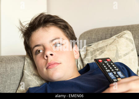 Ragazzo con il telecomando del televisore guardando la TV sul divano teso Foto Stock