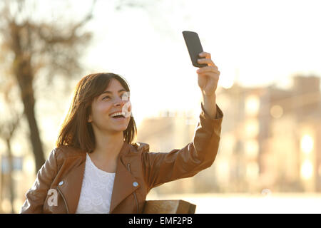 Donna prendendo selfie foto con uno smartphone in inverno seduto su una panchina in un parco Foto Stock