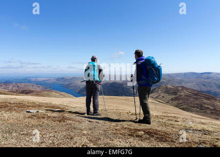 Due escursionisti gode di vista su Ullswater su una soleggiata giornata di primavera dalla collina di pietre bianche Lake District Cumbria Regno Unito Foto Stock