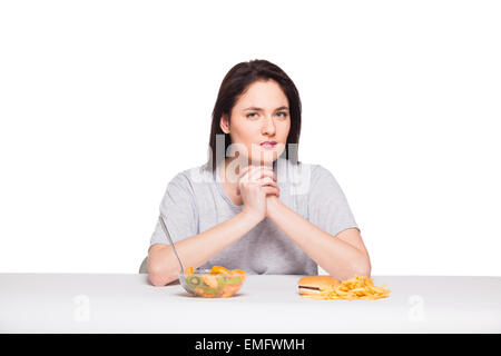 Immagine di donna con frutta e hamburger davanti a pensare a scelta su sfondo bianco, sano versus junk food concept Foto Stock