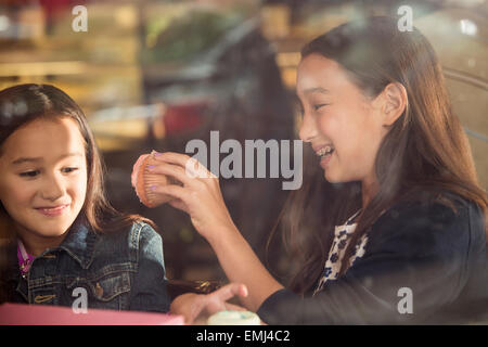 Due sorridenti ragazze giovani mangiare i tortini in Café finestra Foto Stock