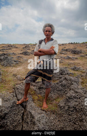 Ritratto di un uomo in piedi su savana rocciosa durante la stagione secca a Sumba, un'isola regolarmente colpita dalla siccità in Nusa Tenggara orientale, Indonesia. Foto Stock