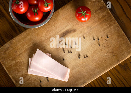 Più fette di Romanian baloney su un tavolo di legno con pomodori ciliegia nel recipiente metallico. Vista superiore Foto Stock