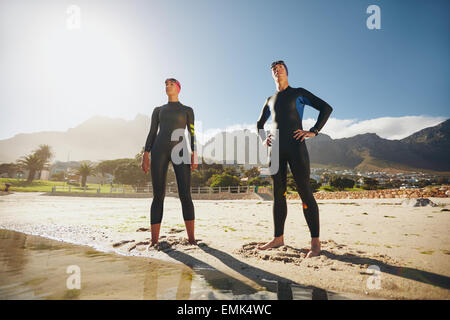 Ritratto di un determinato maschio e femmina triatleti guardando in lontananza. Giovane uomo e donna in piedi presso la spiaggia wearin Foto Stock