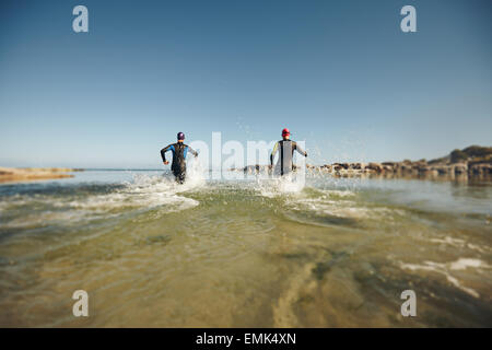 I partecipanti eseguono in acqua per l'avvio di un triathlon. Due triatleti precipitando in acqua per nuotare porzione di gara. Foto Stock