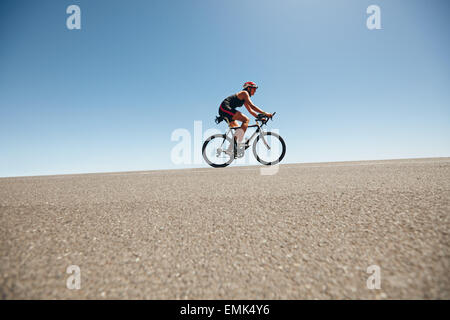 Ciclista femmina su una strada di campagna di formazione per il triathlon. Giovane donna Bicicletta Equitazione su per la collina. Foto Stock