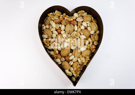 Vari dadi, noci, nocciole, pistacchi, in un cuore ciotola sagomata Foto Stock