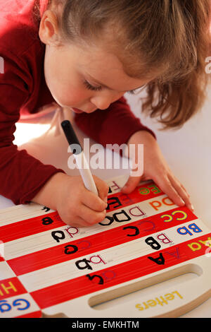 4 anno vecchia ragazza apprendere e mettere in pratica la sua lettere su di un panno pulito prenota Foto Stock