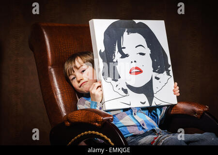 Funny preschooler ragazzo seduto in poltrona con poster, studio Foto Stock