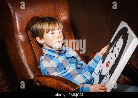 Funny preschooler ragazzo seduto in poltrona con poster, studio Foto Stock