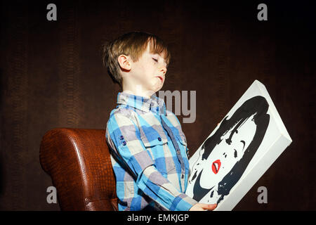 Funny preschooler ragazzo seduto in poltrona con poster, studio Foto Stock