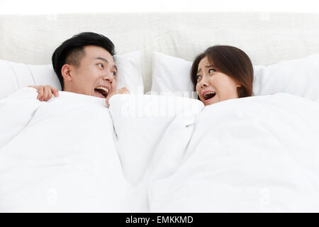 I due giovani uomini e donne nel letto della camera da letto sorpreso gridare Foto Stock