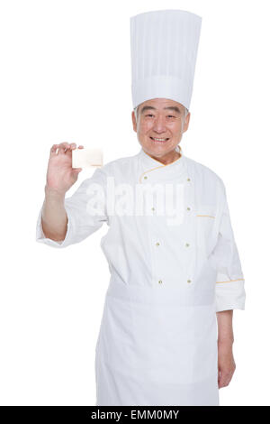 Uomo asiatico che indossa cappello e grembiule da chef sorride come lui  guarda le ciambelle sul tavolo mentre scrivi un notebook mentre si è seduti  in cucina Foto stock - Alamy