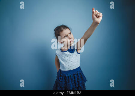Una bambina di sette anni aspetto europeo brunette mantiene ferire le dita oggetto su sfondo grigio, malcontento Foto Stock