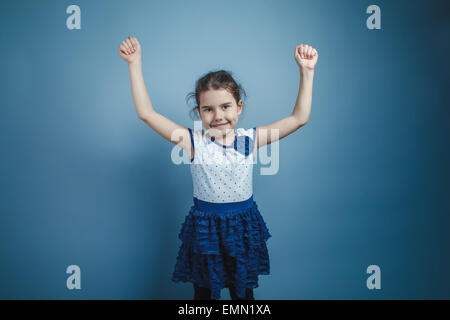 Una bambina di sette anni aspetto europeo brunette sollevate le braccia sorridente su sfondo grigio Foto Stock