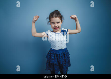 Una bambina di sette anni aspetto europeo brunette sollevate le mani in alto mostra la forza, la potenza Foto Stock