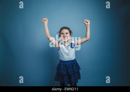 Una bambina di sette anni aspetto europeo brunette mostra i muscoli delle mani su sfondo grigio Foto Stock