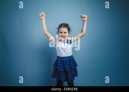 Una bambina di sette anni aspetto europeo brunette mostra la potenza delle mani su uno sfondo grigio, rabbia Foto Stock