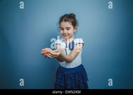 Una bambina di sette anni aspetto europeo brunette sorridente azienda oggetto su sfondo grigio, felicità Foto Stock