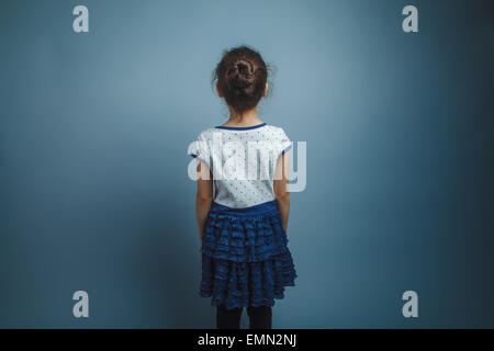 Una bambina di sette anni aspetto europeo brunette ruotato indietro torna vista su sfondo grigio Foto Stock