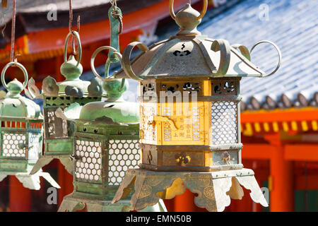 Fila di bronzo lanterne verde appeso dal tetto vermiglio della sala principale presso la famosa Kasuga Taisha Sacrario di Nara, Giappone. Foto Stock