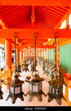 Righe di bronzo verde e oro lanterne pendenti dal tetto vermiglio della sala principale presso la famosa Kasuga Taisha Sacrario di Nara, Giappone. Foto Stock